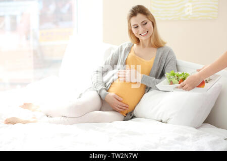 Femmes avec petit-déjeuner pour young pregnant woman resting on bed Banque D'Images