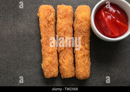 Bâtonnets de fromage frit délicieux et le bol de sauce sur fond gris Banque D'Images