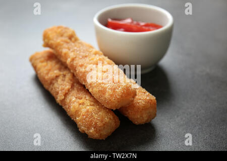 Bâtonnets de fromage frit délicieux et le bol de sauce sur fond gris Banque D'Images