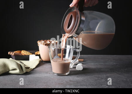 Main de woman pouring cacao jusqu'cup le tableau gris sur fond noir Banque D'Images