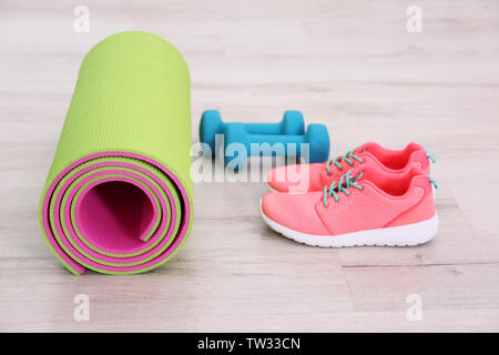 Tapis de yoga avec des baskets et les haltères sur le plancher Banque D'Images