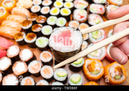 Tenir les doigts baguettes avec nori thon roll over jeu de sushi et de rouleaux sur table en bois Banque D'Images
