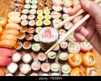 Tenir les doigts avec des baguettes sur rouleau nori thon assortiment de sushi et de rouleaux sur table en bois Banque D'Images