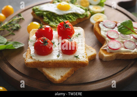 Petit-déjeuner savoureux toasts avec différents légumes sur planche de bois Banque D'Images