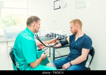 Doctor with stethoscope sphygmomanomètre utilisant contrôle la pression sanguine à un jeune patient dans l'hôpital. Santé, mode de vie sain et Banque D'Images