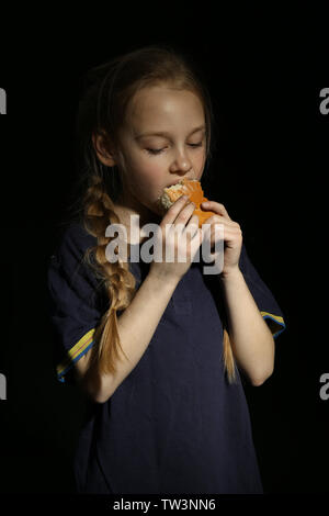 Pauvre petit girl eating bread sur fond noir Banque D'Images