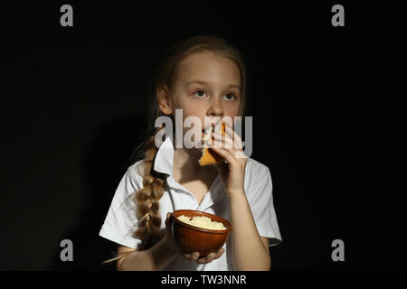 Pauvre petit girl eating bread sur fond noir Banque D'Images