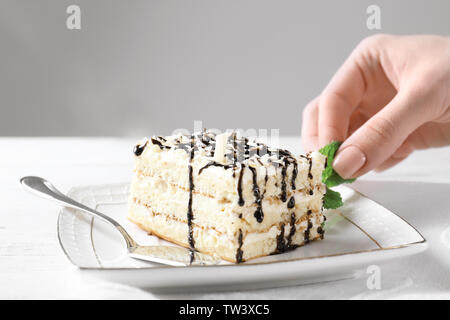 Ajouter les feuilles de menthe main de femme à la plaque avec de savoureux gâteaux et sauce au chocolat sur la table, gros plan Banque D'Images