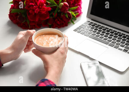 Female hands holding tasse de café sur la table avec l'ordinateur, le téléphone et les pivoines Banque D'Images