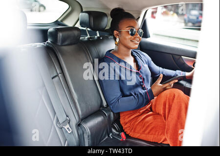 L'entreprise riche femme africaine à siéger à lunettes voiture suv avec des sièges en cuir noir. Téléphone mobile à la main. Banque D'Images