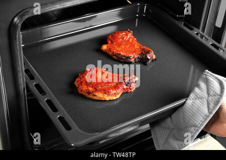 Jeune femme en tenant la plaque de cuisson avec des côtes de porc délicieux hors du four Banque D'Images