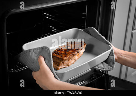 Jeune femme en tenant la plaque de cuisson avec des côtes de porc délicieux hors du four Banque D'Images