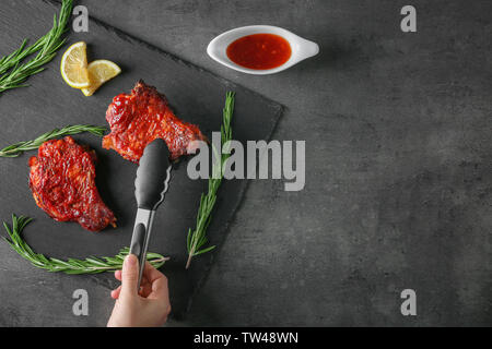 La prise de main de femme avec des côtes de porc sur la plaque en ardoise pinces de cuisine Banque D'Images