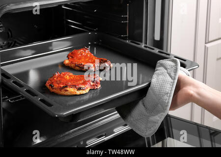 Jeune femme en tenant la plaque de cuisson avec des côtes de porc délicieux hors du four Banque D'Images