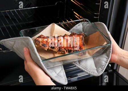 Jeune femme en tenant la plaque de cuisson avec des côtes de porc délicieux hors du four Banque D'Images