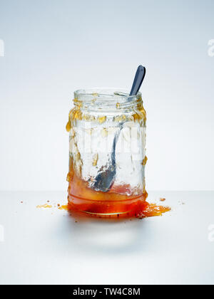 Désordonnée, presque vide pot de confiture d'abricots maison avec cuillère et confiture renversé sur fond blanc Banque D'Images