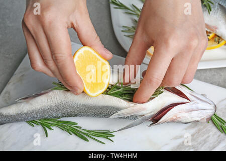 Woman squeezing lemon sur le poisson farci au romarin sur du marbre, closeup Banque D'Images