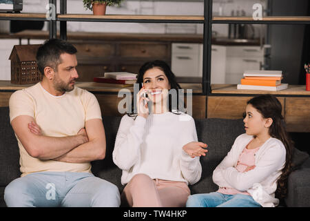 Père et fille offensée assis les bras croisés et à la joyeuse à mother talking on smartphone Banque D'Images