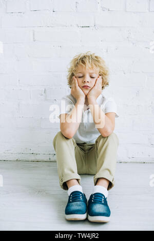 Contrarié preteen boy sitting on floor at home Banque D'Images