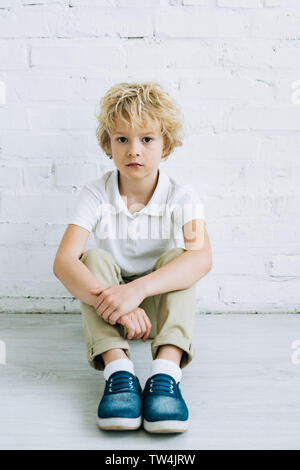 Contrarié preteen boy sitting on floor and looking at camera at home Banque D'Images