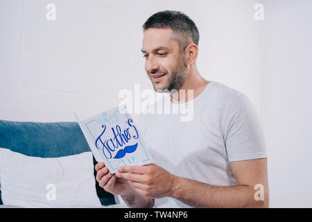 Happy man holding pères jours carte de vœux faits à la main alors qu'il était assis dans la chambre Banque D'Images