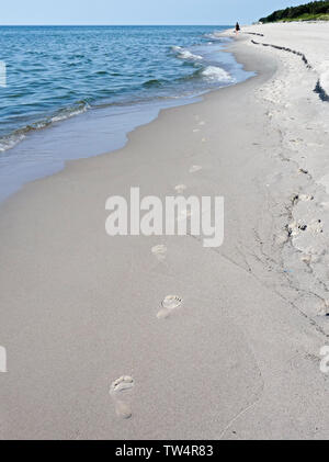 Empreintes de pas sur le sable de la plage disparaissant dans les vagues, dans la distance seule figure humaine marchant le long de la côte Banque D'Images