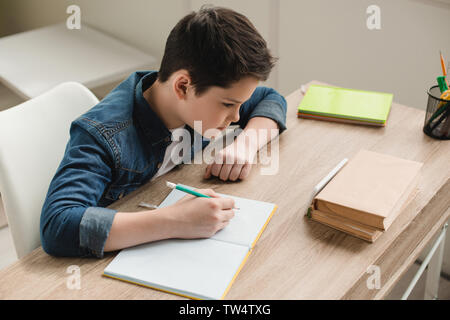 Portrait de garçon attentionné en écriture livre copie tout en faisant le travail scolaire à la maison Banque D'Images