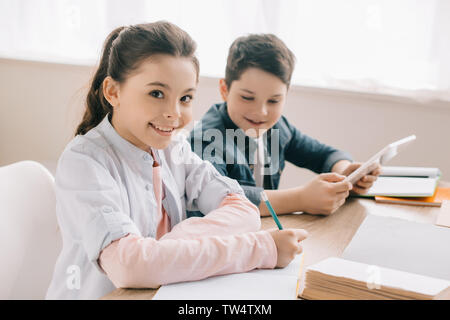 Portrait of smiling enfant écrit dans l'ordinateur portable et à la caméra à tout faire leurs devoirs avec frère joyeux Banque D'Images