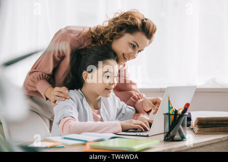 Happy mother helping daughter smiling faisant le travail scolaire à la maison Banque D'Images