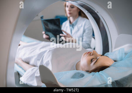 Focus sélectif de radiologue holding x-ray alors que le diagnostic patient couché sur le lit du scanner ct pendant le diagnostic Banque D'Images