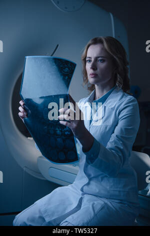 Médecin sérieux à la recherche de x-ray alors qu'il était assis près de diagnostic scanner Banque D'Images