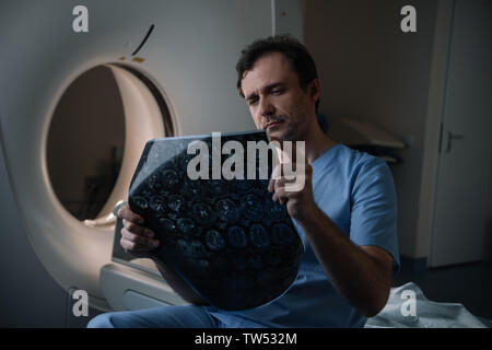 Médecin attentif à la tomographie au diagnostic alors qu'il était assis près de scanner Banque D'Images