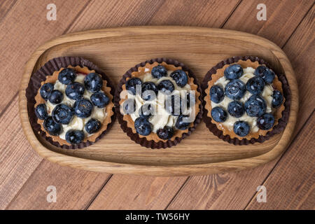 Tartelette aux myrtilles trois sur une plaque de bois sur la table, myrtille, fruits, coquillages cuits avec cupcake blueberry. Banque D'Images