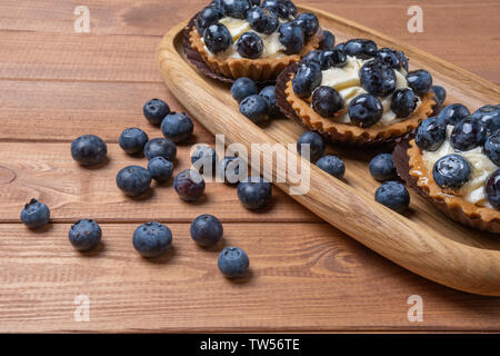 Tartelette aux myrtilles trois sur une plaque de bois sur la table, myrtille, fruits, coquillages cuits avec cupcake blueberry. Banque D'Images