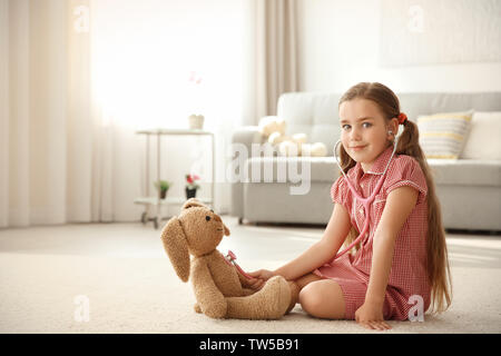 Adorable petite fille examinant bunny jouet avec stéthoscope à la maison Banque D'Images