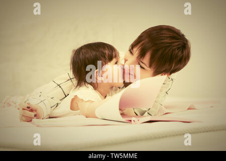 Heureux jeune mère et little baby girl reading a book on bed Banque D'Images