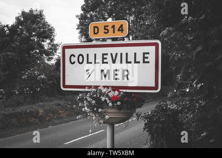 Un panneau indicateur de la ville sur le côté de la route, marquant l'entrée du célèbre village français Colleville sur Mer - pot de fleur suspendu sous Banque D'Images