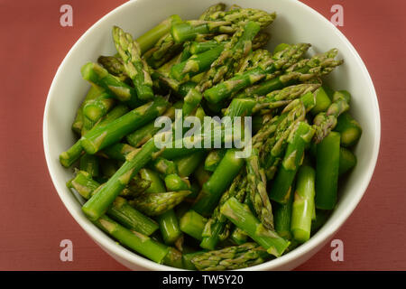 Matières premières asperges fraîchement rincés en tranches dans un bol blanc sur la table rouge Banque D'Images