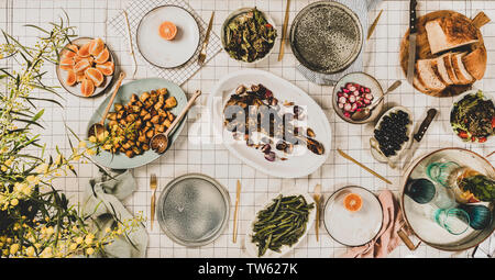 Famille, amis dîner de collecte. Télévision à jeter de l'épaule d'agneau rôti, salades, légumes cuits, des collations, du pain, la limonade en verseuse et son mimosa en fleurs Banque D'Images