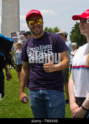 Washington, D.C., USA. 1er juin 2019. Avec le Washington Monument dans le contexte lors de la Marche Nationale pour attaquer le 1er juin 2019, un jeune homme souriant, fait face à l'appareil photo, le port de lunettes et d'une grande Amérique rouge 'Make' baseball cap/hat, et donne une thumbs-up signe devant les mots "socialisme Sucks" sur son t-shirt. La jeune femme à côté de lui, partiellement visible, porte le même cap et sourit légèrement en face vers la gauche. Ils étaient deux de plusieurs pro-Trump à counterprotesters les gens exigent-Action manifestation organisée sur le Washington Monument. Kay Howell/Alamy Banque D'Images