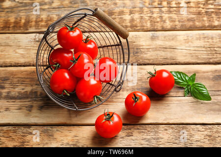 Tomates cerises fraîches dispersées de panier sur table en bois Banque D'Images