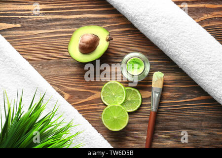 Composition avec masque cosmétique, d'avocat et de tranches de lime sur fond de bois Banque D'Images