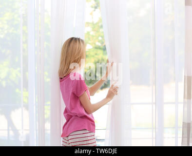 Jeune femme ouvrant rideaux en soie dans la salle Banque D'Images