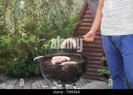 L'homme préparer de délicieuses saucisses sur le gril du barbecue en plein air Banque D'Images