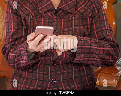 Vieille Femme Asiatique assis et regarder à travers quelque chose sur smartphone moderne, faisant la liaison avec d'autres personnes à la maison, un salon de la technologie, Close up Banque D'Images