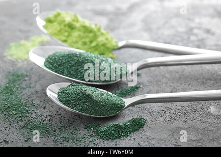 Les cuillères avec la spiruline en poudre et de l'herbe de blé sur fond gris Banque D'Images