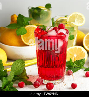 Boisson d'été rafraîchissante de fraises et de canneberges sur une planche de bois blanc, derrière elle sont jaune citron et feuilles de menthe verte Banque D'Images