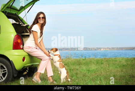 Belle jeune femme avec mignon chien assis dans coffre de voiture en plein air Banque D'Images