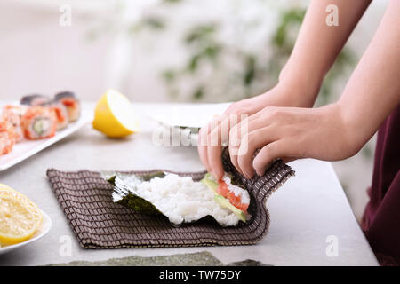 Jeune femme faisant rouleaux de sushi à la maison Banque D'Images