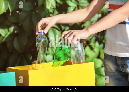 Petit garçon de jeter les bouteilles en plastique dans le récipient extérieur Banque D'Images